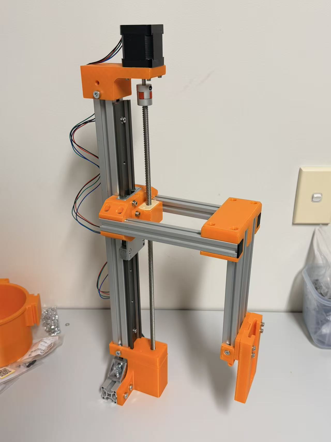 Partially assembled EntoSieve aluminium-extrusion frame with a vertical lead screw, linear stage, motor and orange printed brackets