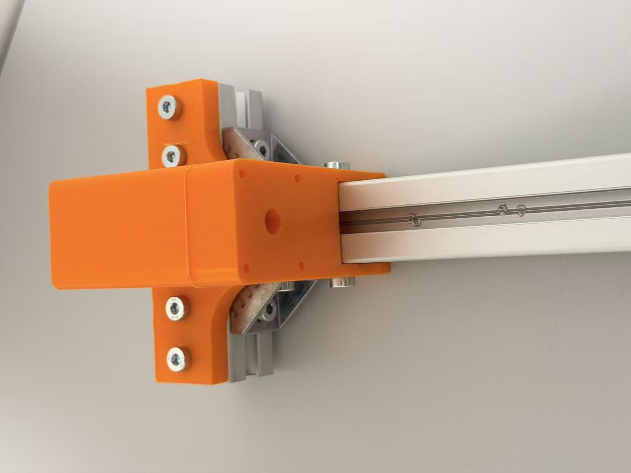 Close-up of an orange printed mounting interface installed around a horizontal aluminium extrusion